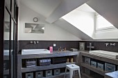 Open-fronted, grey concrete shelves with integrated sinks in bathroom with sloping ceiling