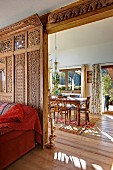 Artistically carved wooden wall as partition between red sofa in living area and sunny dining area in prefabricated house