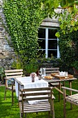Wooden table and chairs in garden outside stone house with ivy-covered façade