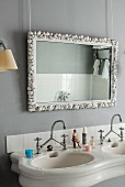Vintage-style twin sinks with vintage-style tap fittings below mirror with frame decorated with seashells