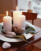 Dekorativer Teller mit brennenden weissen Kerzen, Steinen und Blättern
