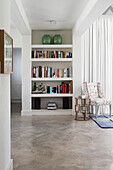 White built-in shelving with books and green vases, armchair with floral pattern