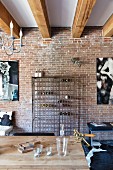 Metal wine rack against brick wall and wooden table in interior with wood-beamed ceiling