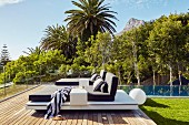 Modern loungers with cushions on terrace amongst palm trees