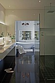 Spotlights in ceiling, mirrored cabinet with indirect lighting and chandelier above bathtub in modern bathroom with walk-in shower