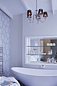 Chandelier above free-standing, designer bathtub; shelves in niche with mirrored wall