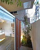 Schmaler Pflanzstreifen zwischen Mauer und verglaster Eingangsfassade einer japanischen Konditorei