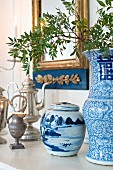 Antique silver jugs, blue and white china pot and vase on shelf below gilt-framed mirror on wall