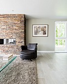 Leather armchair on pale grey flokati rug in front of fireplace in stone chimney breast in modern interior