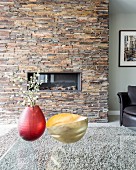 Flowering branches in red vase and gold dish on glass table in front of fireplace in stone-clad chimney breast