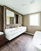 Elegant bathroom painted pale brown with large floor tiles and long, white washstand on wall