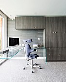 Office chair at L-shaped glass table next to fitted cupboards with grey and brown striped veneer in elegant study