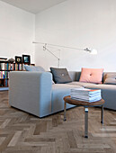 Stool with leather cushion and stacked magazines next to grey sofa