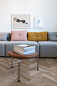 Stool with leather cushion and stack of magazines in front of modern sofa