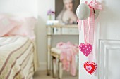 Pink hearts on ribbons hanging from doorknob and view into romantic bedroom