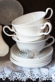 White china cups and saucers and speckled feather on lace shelf cover in antique cabinet