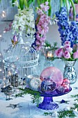 Kuchenständer aus Glas mit Weihnachtskugeln vor Blumendeko mit Hyazinthen und Rosen in Bauernsilber-Vase