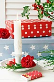 Kerzenständer mit Rosenblüte und adventlicher Streichholzschachtel; Geschenkeboxen im Hintergrund