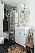 Simple washstand below round mirror on white-tiled wall in bathroom with bathtub behind curtain
