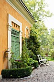 Bench and table on gravel terrace outside yellow limewashed country house with green wooden door