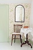 Chair with turned legs, white lace cloth on dark wood side table and mirror on wallpapered wall in corner