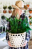 Frau mit Strohhut hält Grünpflanze in Übertopf
