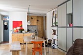 Essbereich mit schlichter Holzbank und orangefarbenem Stuhl um Tisch, seitlich Einbauschrank mit hellgrauer Front in moderner Küche