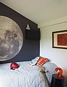 Ausschnitt eines Einzelbettes mit hellgrauem Plaid, vor dunkelgrau getönter Wand mit Abbildung eines Planeten im Jugendzimmer