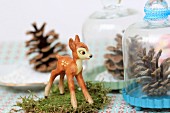Winter arrangement of fawn figurine on moss & pine cone under glass cover