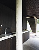 Minimalist kitchen with dark wooden fronts, concrete column and glass wall