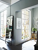 Offener Wohnbereich mit raumhohen Sprossenfenstern, an Wand Standspiegel in einer Loft-Wohnung