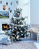 White decorations and blue baubles on Christmas tree in living room with fireplace