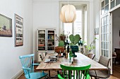 Cacti on dining table and coloured wooden chairs below pendant lamp with lampshade made from leaves of veneer