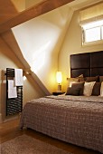Double bed with headboard in attic niche with window and heated towel rail on wall