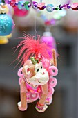 Monkey toy with feminine clothing hanging from string of colour beads as Christmas decoration