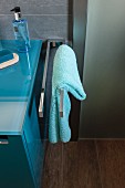 A turquoise towel on a stainless steel towel rail next to a washstand in a modern bathroom