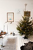 Decorated Christmas tree on white wooden floor, toys on table in front of retro standard lamps