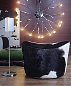 Cow-hide pouffe and designer standing ashtray in front of retro wall lamp