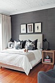 Dog lying on double bed with scatter cushions in modern bedroom with stucco ceiling and black wallpaper