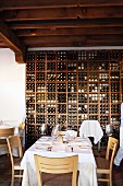 Weiß gedeckter Restauranttisch vor hohem Weinregal unter dunkler Balkendecke