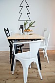 Dining table and various black and white chairs in front of outline of Christmas tree on wall