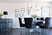 Grey upholstered chairy around round table below suspended bulb-style pendant lamps in open-plan living area with breakfast bar