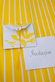 Invitation cards with yellow floral motif on white envelope on yellow and white striped surface