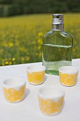 White beakers with yellow, retro pattern and flask of spirits on white surface outdoors
