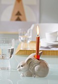 A candle holder and a burning candle stuck onto a porcelain rabbit