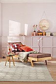 A comfortable 1950s-style lounger with cushions and throw, a side table on a patterned rug and a sideboard and a wall painted pastel purple