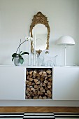 Sideboard with smooth white front and open-fronted firewood store, retro lamp with hemispherical lampshade and antique mirror on wall