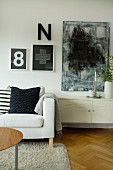 Sofa mit Dekokissen neben niedrigem Metallspind, schwarz-weiße abstrakte Kunst und Typo-Deko an der Wand