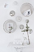 White, festive wall decorations above candelabra and glass vase on side tablee