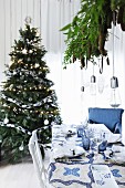 Christmas dinner table set in blue and white in front of Christmas tree